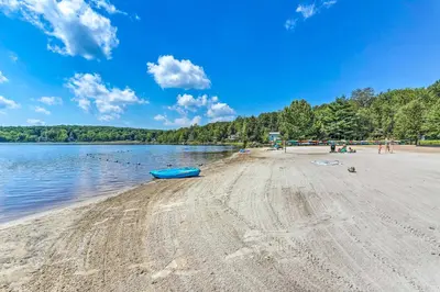a beach with a blue boat on the shore at Lakefront Poconos Family Home with Pool Access in Pocono Lake