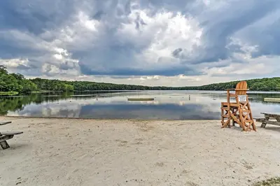 a beach with two chairs and a bench and a lake at Family-Friendly Big Bass Lake Vacation Rental! in Gouldsboro