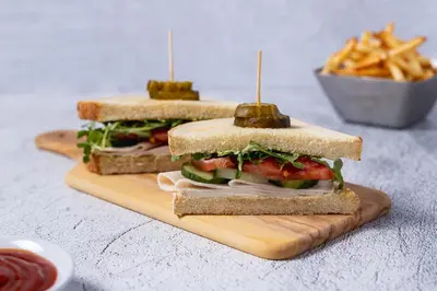 two sandwiches on a cutting board with a bowl of fries at Hyatt Place Secaucus Meadowlands in Secaucus