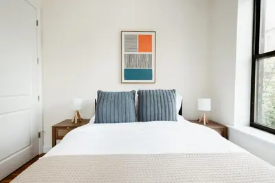 a white bed with two blue pillows in a bedroom at Spacious 3BR Upper West Side Apt - Steps from Central Park in New York