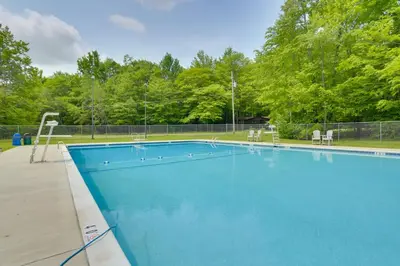 a large blue swimming pool with chairs and trees at Game Room, Hot Tub and Fire Pit Pocono Lake Escape! in Pocono Lake