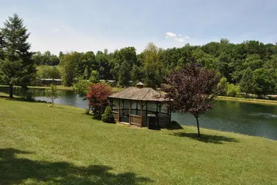 a gazebo in the grass next to a lake at Robin Hill Camping Resort Deluxe Cottage 13 in Lenhartsville