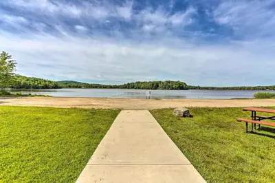 a park bench sitting on the grass near a body of water at Romantic Pocono house - stream, lake, beach, pool, firepit in Locust Lakes Village